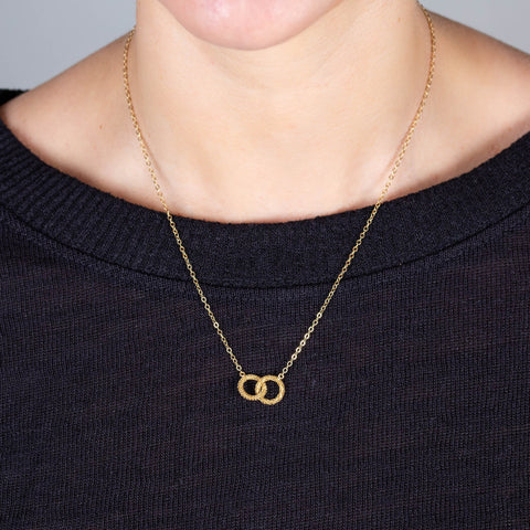 A model wears a short pendant with two interlocking 18k yellow gold circles that is set in a delicate chain.