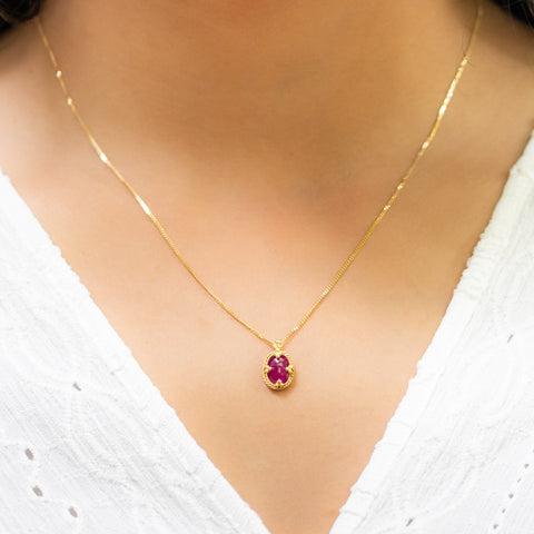 A model wears this oval Ruby pendant on an 18K yellow gold chain. Handmade gold bezel features braided detail and granulated prongs.