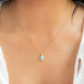 A model wears an 18K yellow gold pendant with Ethiopian Opal. Iridescent colors include green, blue, and pink. Handmade frame with braided accents.