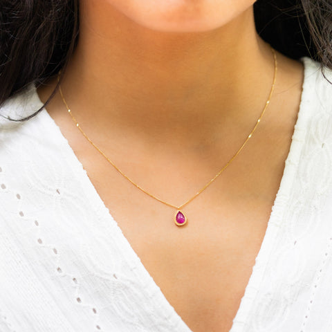 A model wears a ruby teardrop pendant in 18K yellow gold, suspended from a handmade gold bezel with braided detail on an 18K yellow gold chain. Handmade in New York. 