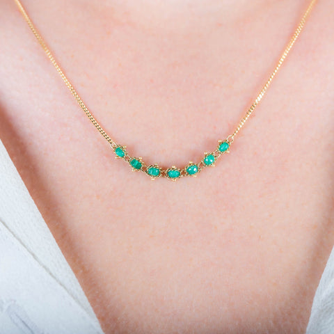 A close-up of a delicate 18k yellow gold chain necklace that features a row of woven emerald beads in the center