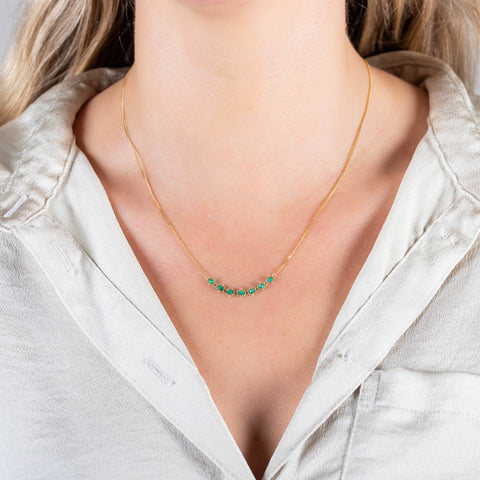 A model wears a delicate 18k yellow gold necklace with a row of woven emerald beads in the center.
