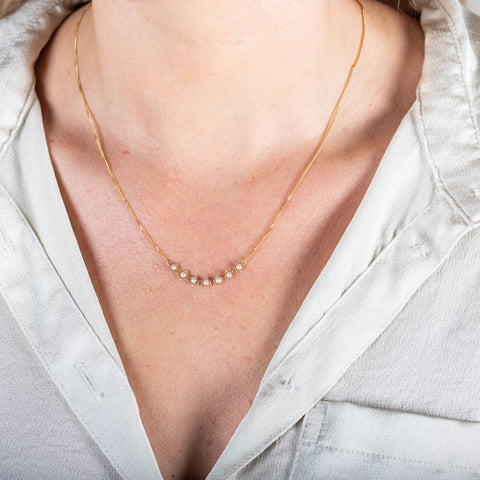 A close-up of a delicate 18k yellow gold chain necklace that features a row of woven pearl beads in the center