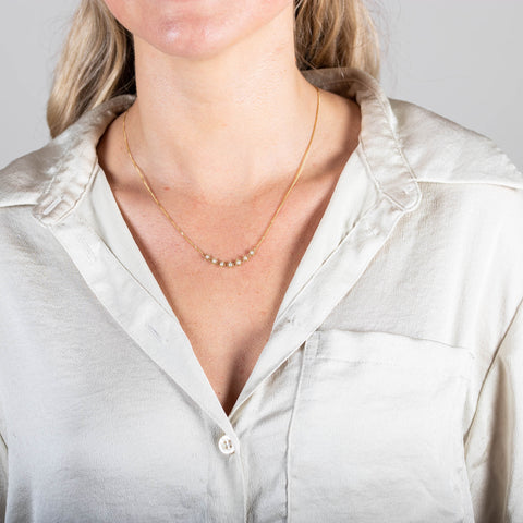 A model wears a delicate 18k yellow gold necklace with a row of woven pearl beads in the center.
