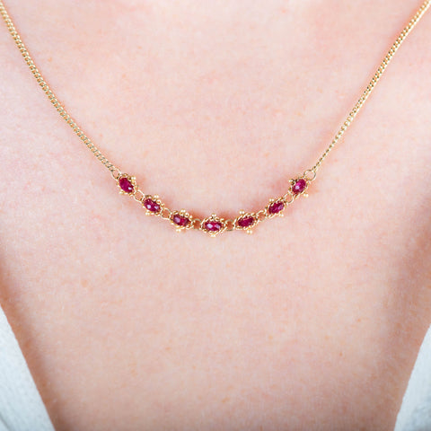 A close-up of a delicate 18k yellow gold chain necklace that features a row of woven ruby beads in the center