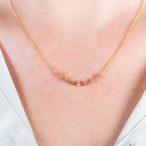 A close-up of a delicate 18k yellow gold chain necklace that features a row of woven spinel beads in the center