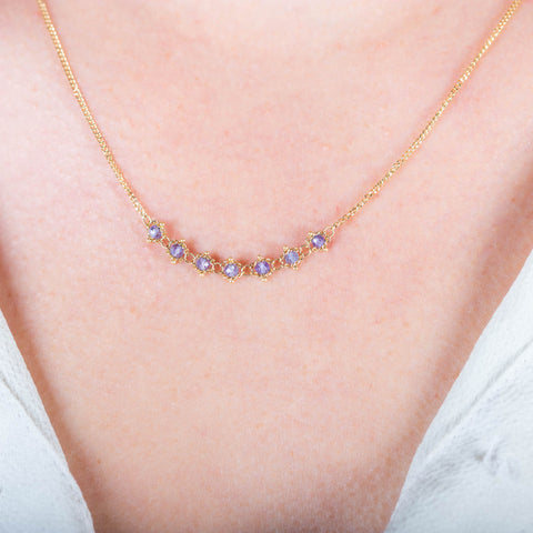 A close-up of a delicate 18k yellow gold chain necklace that features a row of woven tanzanite beads in the center