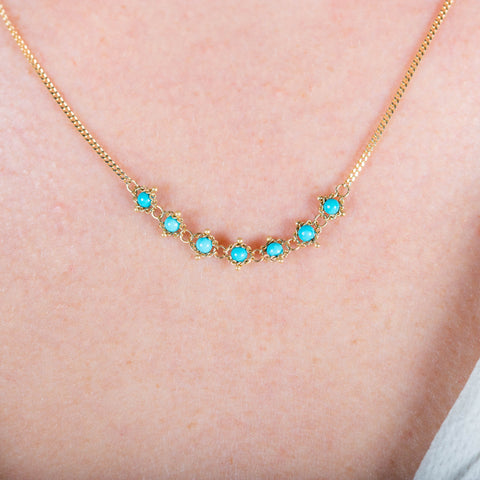 A close-up of a delicate 18k yellow gold chain necklace that features a row of woven turquoise beads in the center