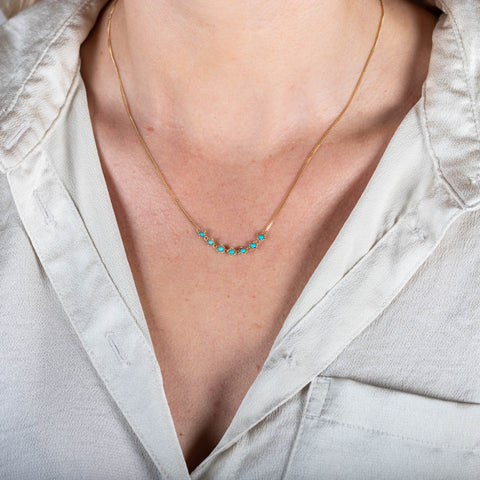 A model wears a delicate 18k yellow gold necklace with a row of woven turquoise beads in the center. 