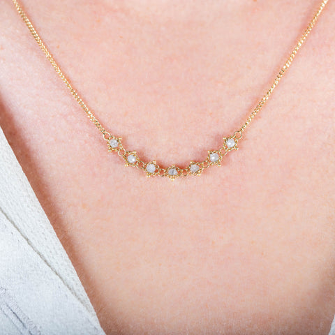 A close-up of a delicate 18k yellow gold chain necklace that features a row of woven silver diamond beads in the center
