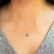 A  model wears a rectangular Boulder Opal pendant set in 18k yellow gold bezel, suspended from an 18K yellow gold chain. Opal displays mesmerizing neon greens and blues, set in a unique one-of-a-kind design with braided detail.