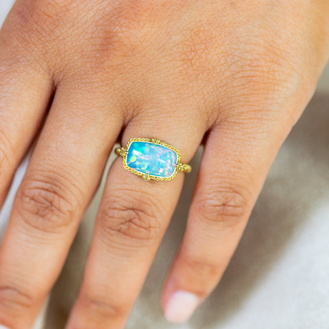 A model wears this Ethiopian Opal ring in 18K yellow gold, highlighting its organically shaped rectangular opal. Meticulously handmade gold frame with intricate braided detail and granulations. Handmade in New York. 