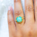A model wears this Ethiopian Opal ring in 18K yellow gold, boasting bold flashes of electric green and neon yellow over sparkling turquoise. Handmade gold frame showcases braided detail and granulated prongs. Handmade in New York. 