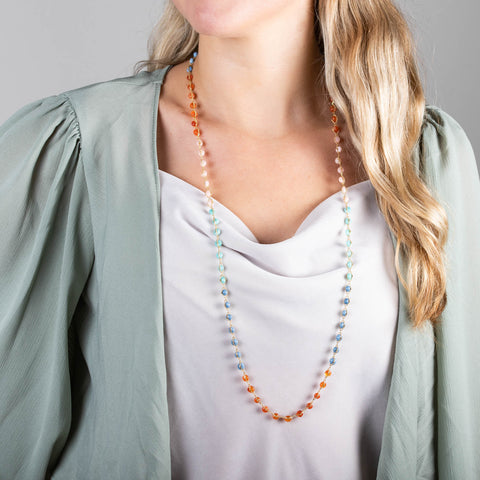 A model wears a long necklace featuring amazonite, sunstone, blue and pink opal beads threaded with 18k yellow gold chain.