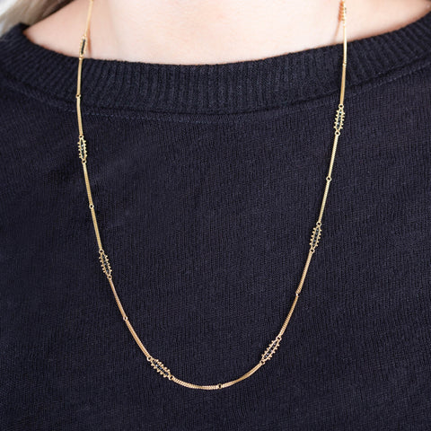 A model wears a long 18k yellow gold chain necklace with rows of black diamond stations placed throughout the chain.