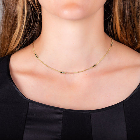 A model wears a short 18k yellow gold chain necklace with rows of black diamond stations woven throughout.