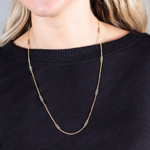 A model wears a long 18k yellow gold chain necklace with rows of blue diamond stations placed throughout the chain.