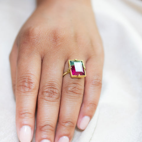 A model wears an 18K yellow gold Tourmaline ring with color variation. Green and raspberry pink hues resemble watermelon. Set in 18K gold with handmade prongs.