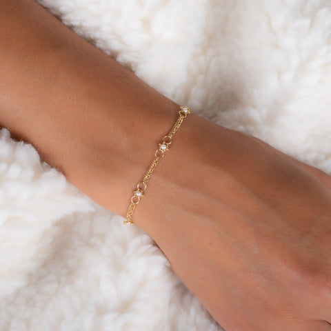 A close up of a delicate 18k yellow gold chain bracelet that is dotted with pearl bead stations throughout.