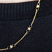 A close-up of a delicate woven 18k yellow gold chain necklace with a white pearl bead station.