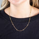 A model wears a long 18k yellow gold chain necklace dotted with white pearl beads throughout.
