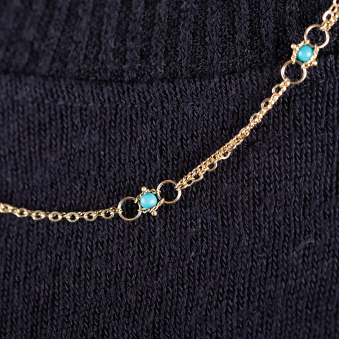 A close-up of a delicate woven 18k yellow gold chain necklace with a turquoise bead station.