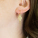 A model wears an 18k yellow gold earring crafted with white pearls woven into a diamond shaped lattice pattern and has three dangling chains at the bottom.