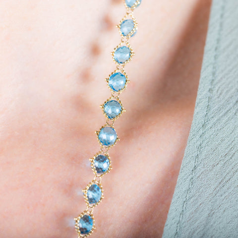 A close-up of a woven 18k yellow gold with London blue topaz beads throughout