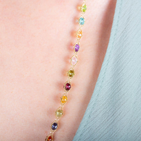 A close-up of a multi-colored woven gemstone necklace featuring Sunstone, Peridot, Aquamarine, Lolite, Apatite, Imperial Topaz, Rhodolite Garnet, Morganite, Tanzanite, Amethyst, and Grossular Garnet