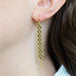 A close up of a pair of long champagne diamond earrings which feature a woven lattice pattern and two dangling chains at the bottom of the earring. The earrings fasten with french hook closures.