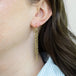 A model wears a pair of long champagne diamond earrings which feature a woven lattice pattern and two dangling chains at the bottom of the earring. The earrings fasten with french hook closures.
