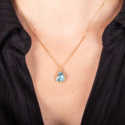 An angular shaped turquoise stone with dark brown veins is set in 18k yellow gold and hangs from a short chain.