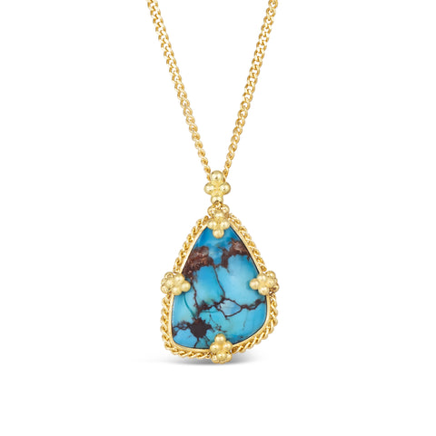 An asymmetric turquoise stone with dark brown veins is set in 18k yellow gold with braided details and four granular prongs.