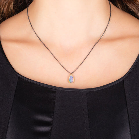 A close-up of a model wearing an oxidized sterling silver chain with 18k yellow gold and opal pendant.