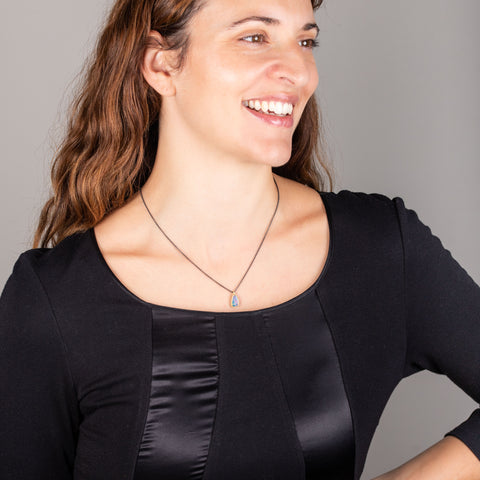 A model in a black scoop-neck top wears an 18k gold and oxidized sterling silver necklace with an opal pendant.
