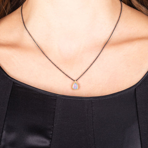 A small Australian Opal pendant with blue and pink hues is set in 18k yellow gold and hangs on an oxidized sterling silver chain.
