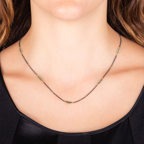 An oxidized sterling silver chain is set with stations of blue diamonds set in 18k yellow gold.