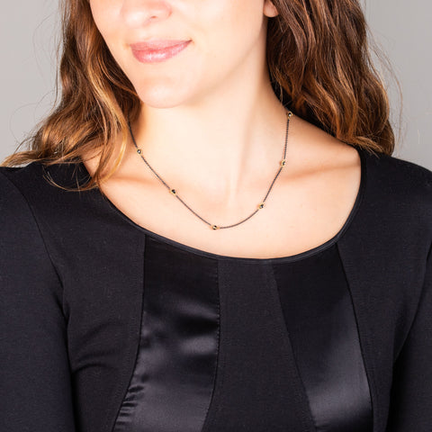A model wears a short black diamond station necklace with 18k yellow gold bezels and set throughout an oxidized sterling silver chain.