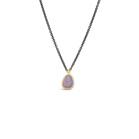 A small australian opal pendant with blue and pink hues is set in 18k yellow gold bezel and hangs on an oxidized sterling silver chain.