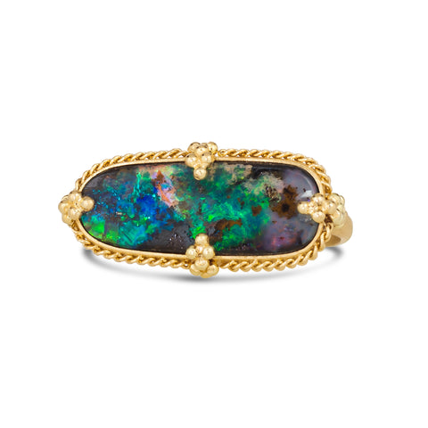 A ring with a large rectangular opal with green, blue, purple and black hues, is set in an 18k yellow gold chain wrapped bezel. The ring sits on a thin band and features four granulated prongs.