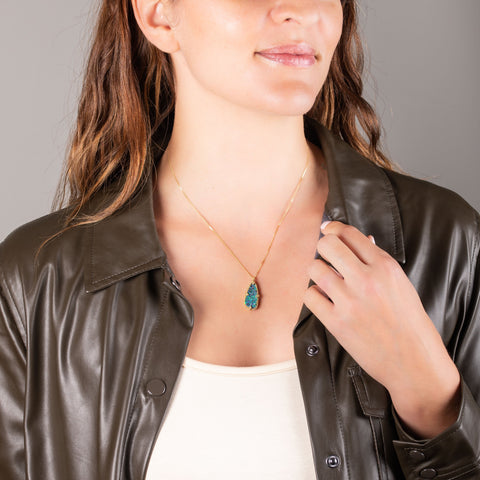 A model wears a large teardrop shaped opal set in 18k yellow gold wrapped in chain with four beaded prongs and hangs from a delicate chain.
