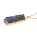 A side view of a large carved Andamooka opal, with dark purple, green and blue hues, that has a delicate scalloped edge motif. The pendant is set in an 18k yellow gold chain wrapped bezel and hangs on a delicate long chain.