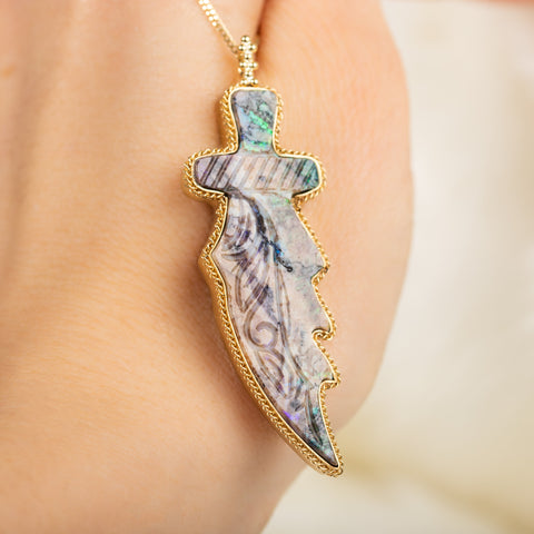 A large andamooka opal stone is carved into the shape of a dagger and set in an 18k yellow gold chain wrapped bezel. The pendant hangs on a long delicate chain.