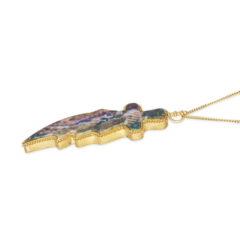 A side view of a large andamooka opal stone, which is carved into the shape of a dagger and set in an 18k yellow gold chain wrapped bezel. The pendant hangs on a long delicate chain.