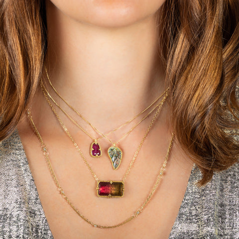 A model wears four layered necklaces, including a small ruby pendant, a carved leaf pendant, a rectangular tourmaline pendant and a diamond chain.