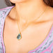 A model wears an andamooka opal, with blue and black hues, that has a skull carved into the stone. The pendant is set in an 18k yellow gold chain wrapped bezel with four beaded prongs and hangs on a delicate short chain.