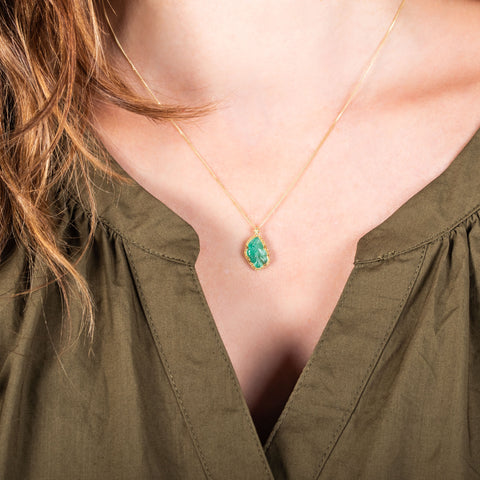 A small emerald pendant is carved into a leaf and is set in an 18k yellow gold bezel on a delicate chain.