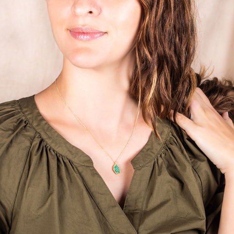 A model wears a small leaf shaped emerald pendant that is set in 18k yellow gold and hangs from a delicate short chain.