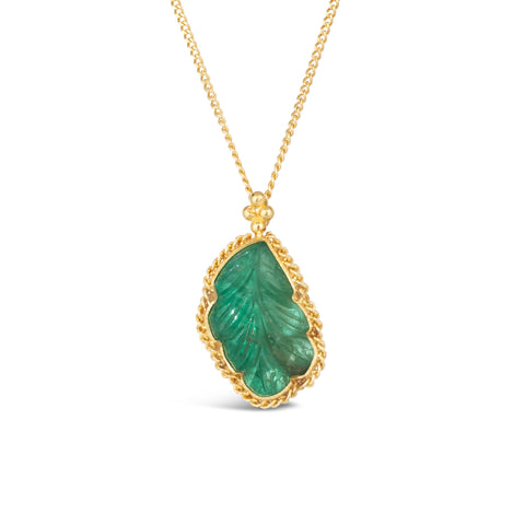 A small emerald pendant carved into the shape of a tropical leaf is set in a chain wrapped 18k yellow gold bezel and hangs on a delicate chain.