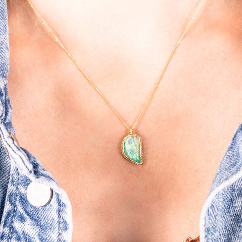 An Ethiopian opal pendant carved into the shape of a leaf is set in an 18k yellow gold chain wrapped bezel and hangs from a delicate chain.